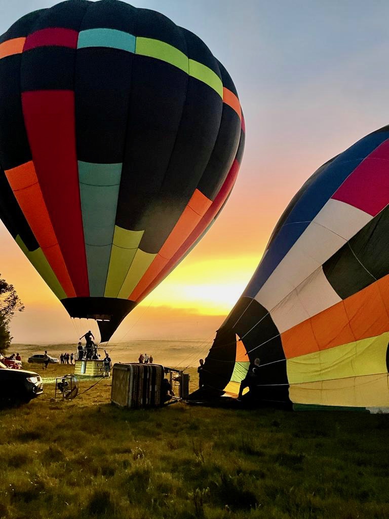 Dois balões da Cambará Balonismo sendo preparados para decolagem ao pôr do sol