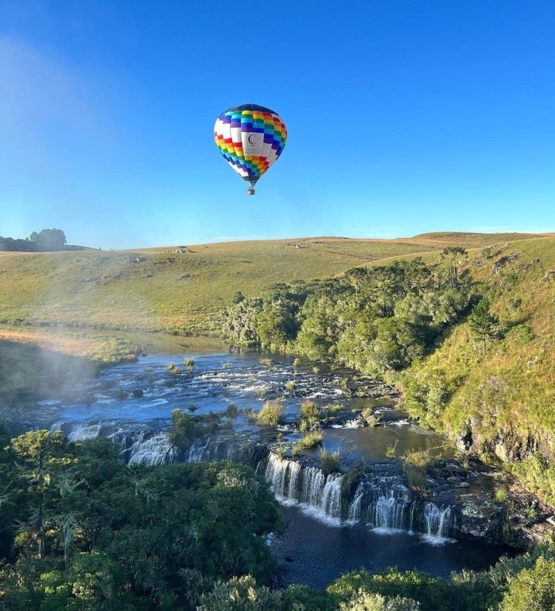 Balão colorido sobrevoando cachoeira e mata nativa em Cambará do Sul